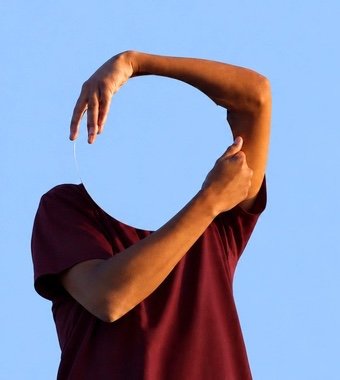 Pessoa de camiseta bordô segurando um espelho redondo diante do rosto, refletindo o céu
